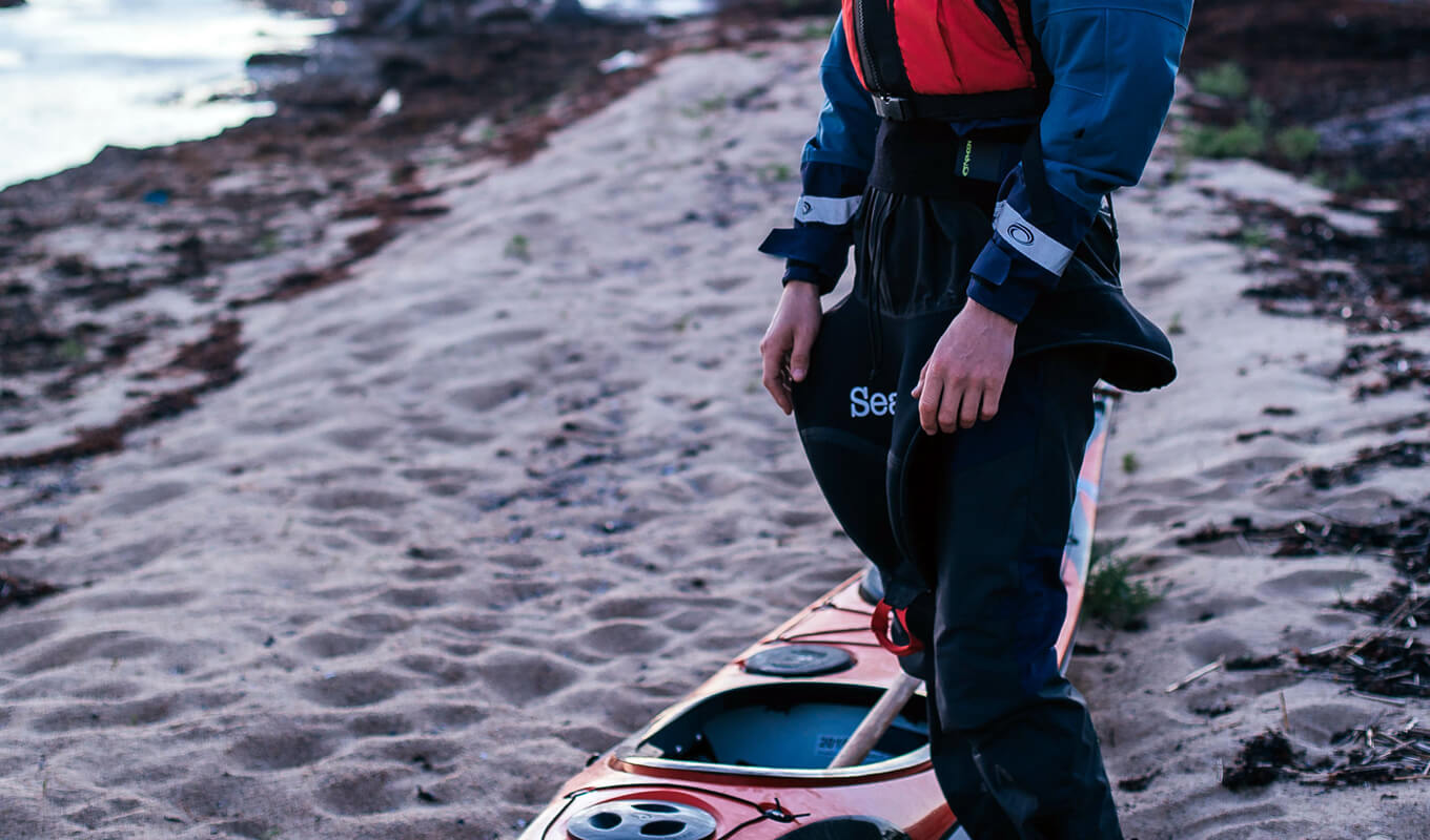 Man standing next to a kayak while wearing a sprayskirt