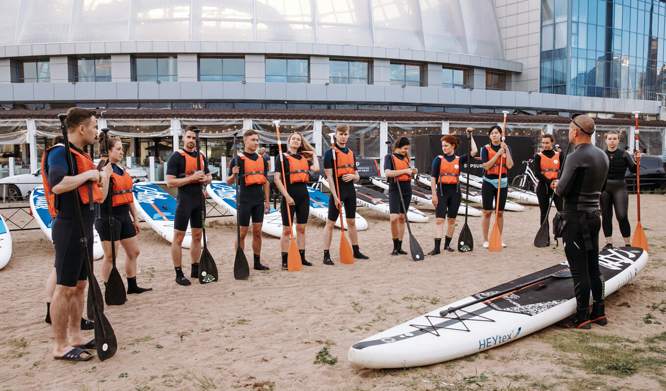 Man on a black wetsuit teaching a group of people how to paddle board