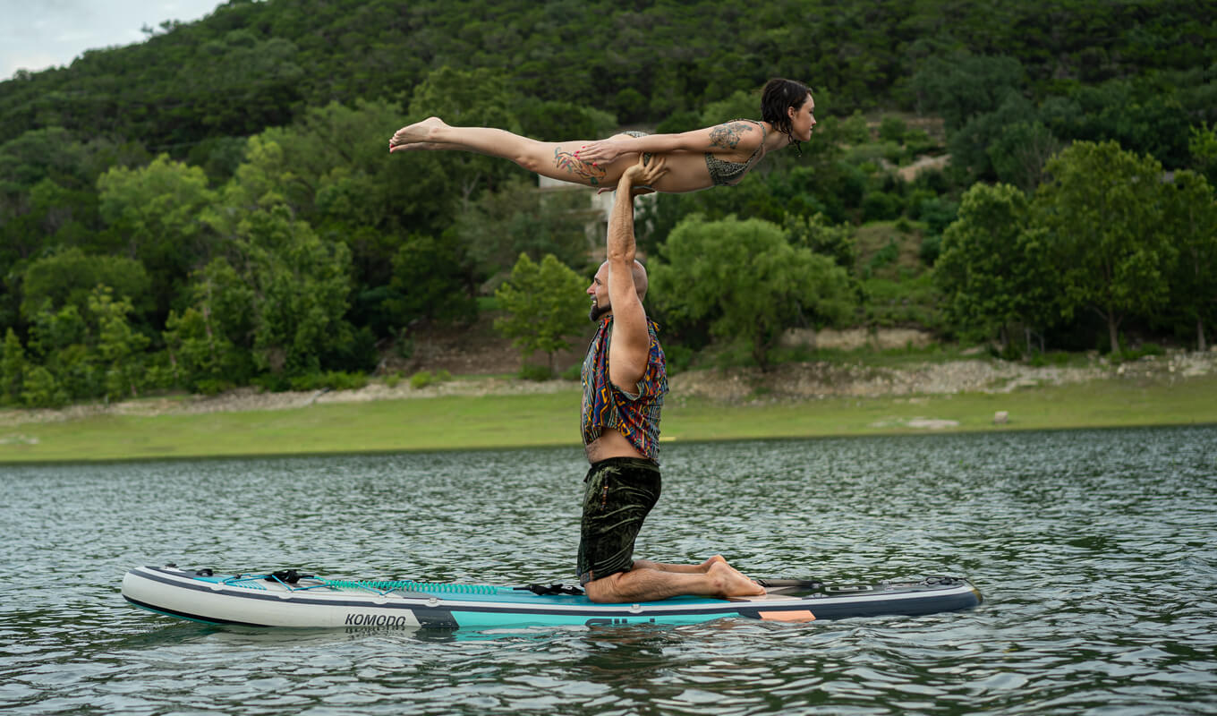 Man lifting a woman performing yoga while on a GILI paddle board